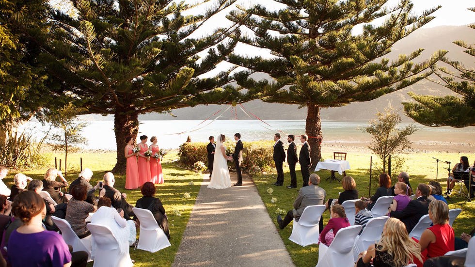 A bride and groom share their vows during a wedding ceremony at Furneaux Lodge with Endeavour Inlet background in the Marlborough Sounds in New Zealand's top of the South Island