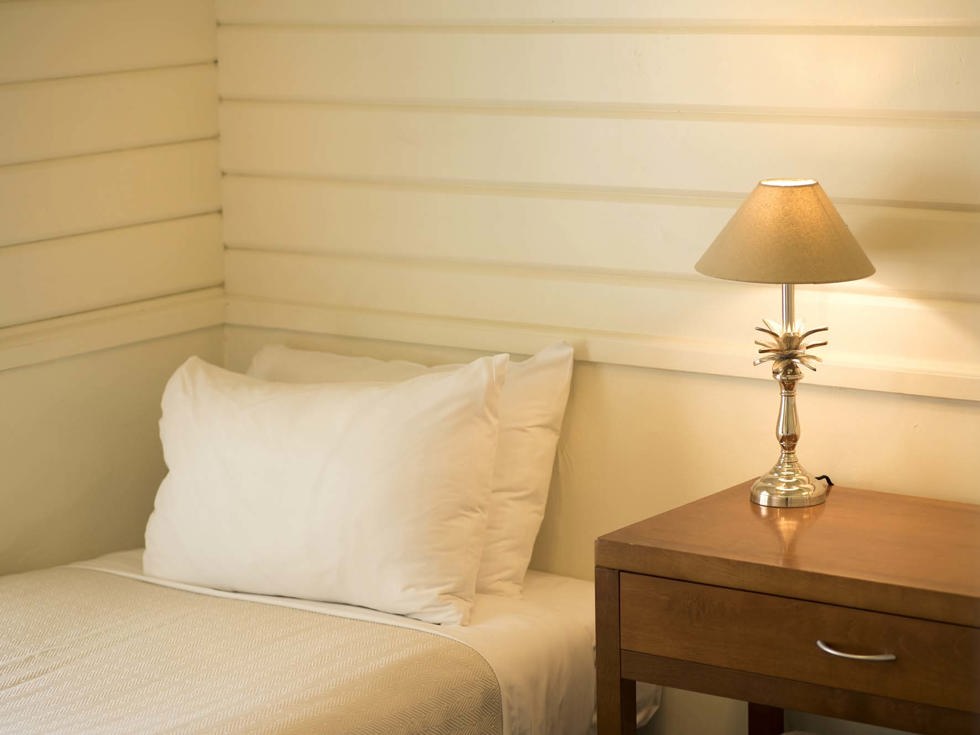 A single bed in a Cook's Cottage with natural decor details at Furneaux Lodge in the Marlborough Sounds at the top of New Zealand's South Island.