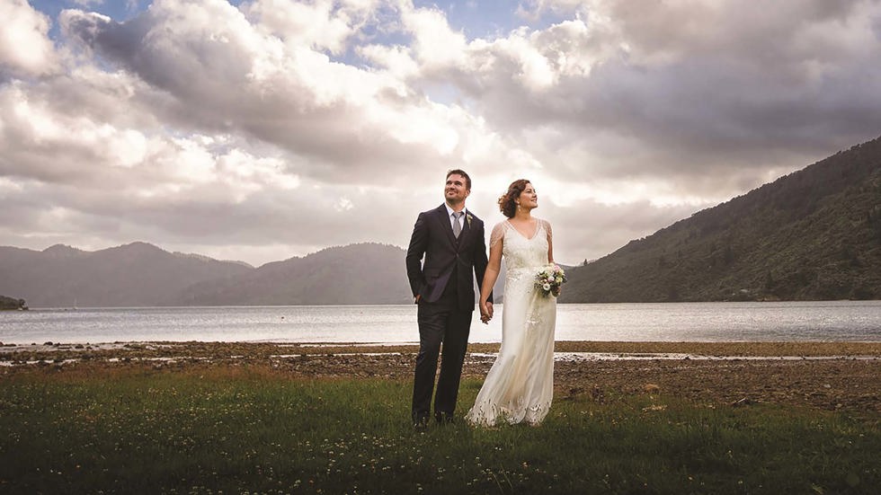 A couple stand together with a scenic Endeavour Inlet background in the Marlborough Sounds in New Zealand's top of the South Island