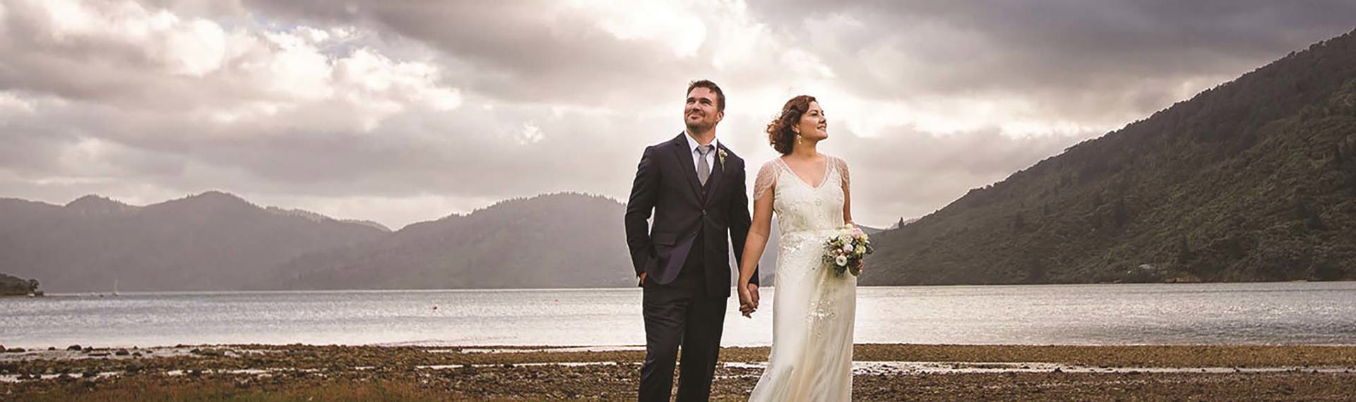 A couple stand together with a scenic Endeavour Inlet background in the Marlborough Sounds in New Zealand's top of the South Island