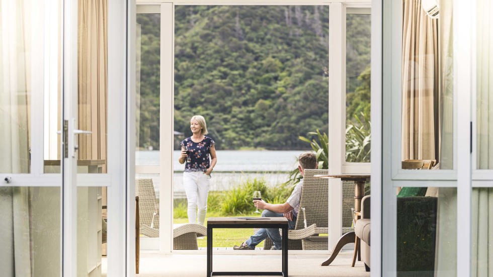 A couple enjoy glasses of wine on their private Endeavour Suite deck at Furneaux Lodge in the Marlborough Sounds at the top of New Zealand's South Island.