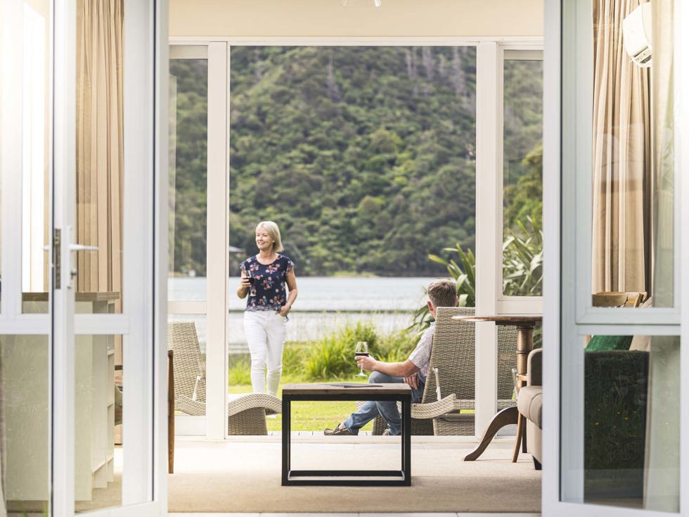 A couple enjoy glasses of wine on their private Endeavour Suite deck at Furneaux Lodge in the Marlborough Sounds at the top of New Zealand's South Island.