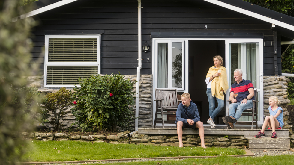 A family of four relax on the private deck of a Cook's Cottage at Furneaux Lodge in the Marlborough Sounds, New Zealand.