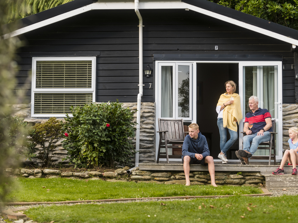 A family of four relax on the private deck of a Cook's Cottage at Furneaux Lodge in the Marlborough Sounds, New Zealand.