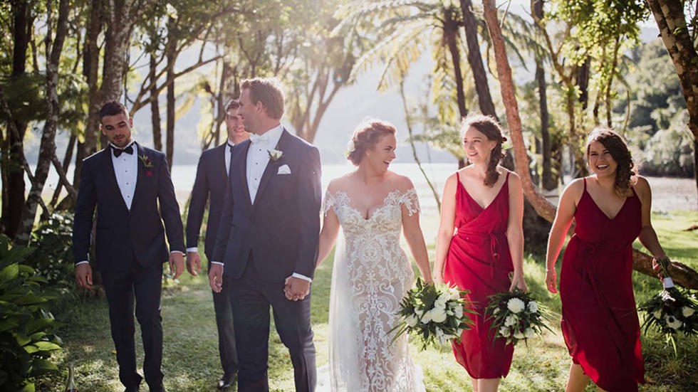 A bride, groom and wedding party walk through the native trees by the beach at Furneaux Lodge in the Marlborough Sounds in New Zealand's top of the South Island