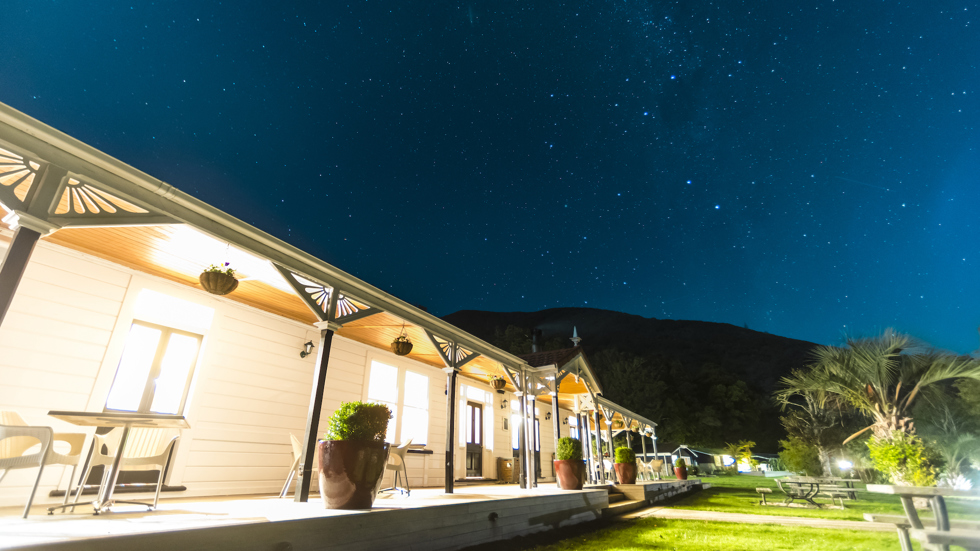 A view at night along the verandah of historic Howden House with lights on and stars in the sky, in the Marlborough Sounds at the top of New Zealand's South Island.