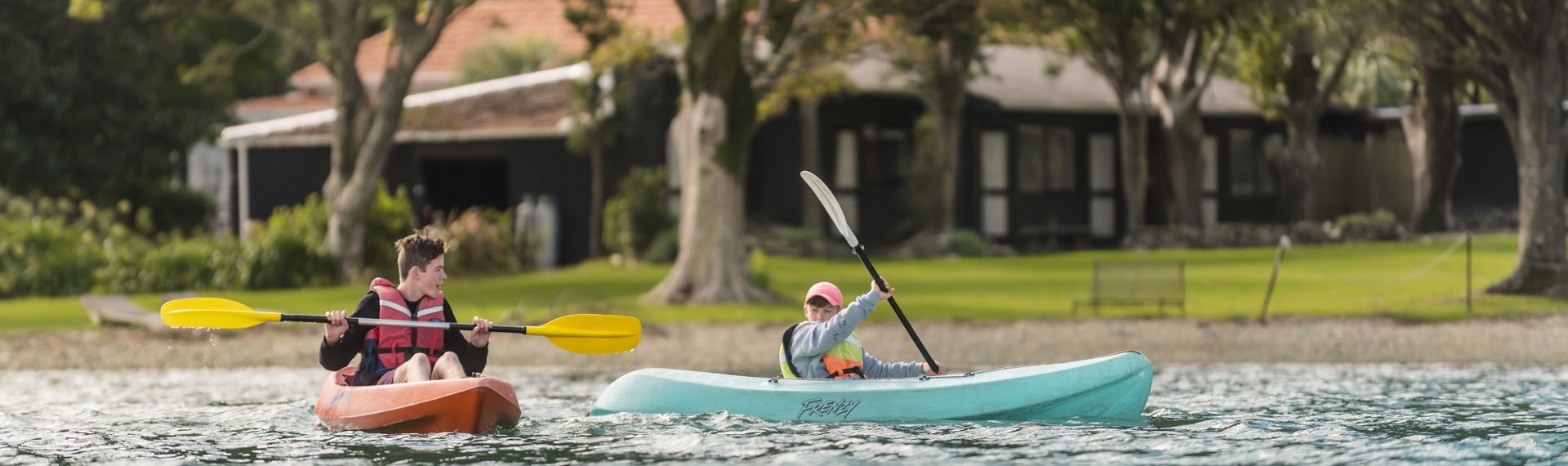 Two boys paddle kayaks in front of Furneaux Lodge in New Zealand's Marlborough Sounds.