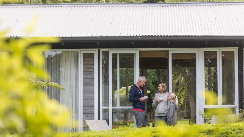 A family of three relax with hot drinks outside an accommodation room at Furneaux Lodge in the Marlborough Sounds, New Zealand.