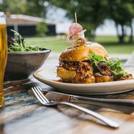 Gourmet chickpea and pumpkin burger with potatoes and side salad served with ocean view and a pint of beer at the Furneaux Lodge Restaurant in the Marlborough Sounds at the top of New Zealand's South Island.