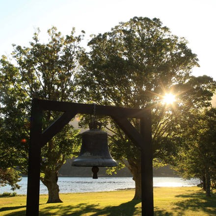 A bell on the lawn under the trees on the waterfront at Furneaux Lodge, in the Marlborough Sounds at the top of New Zealand's South Island.