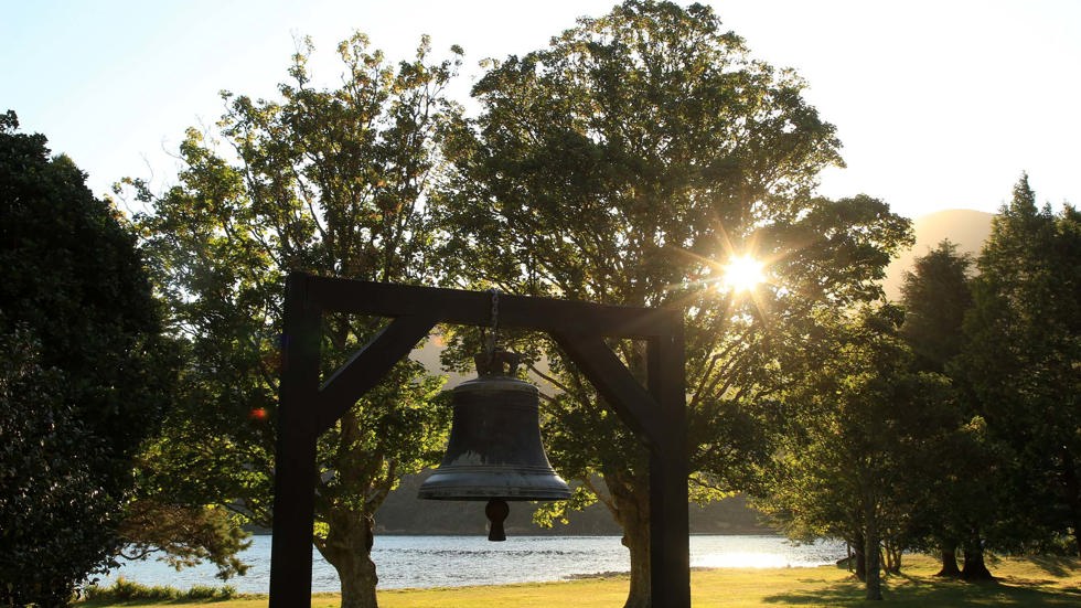 A bell on the lawn under the trees on the waterfront at Furneaux Lodge, in the Marlborough Sounds at the top of New Zealand's South Island.