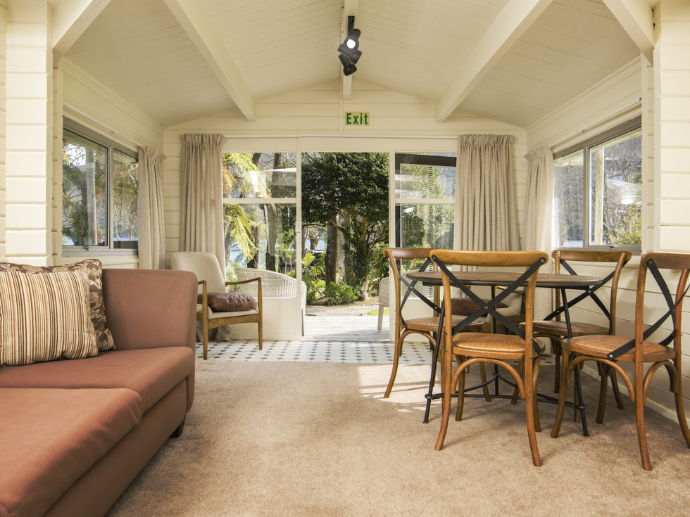 A Cook's Cottage lounge and dining area looking out over the Furneaux Lodge grounds at Furneaux Lodge in the Marlborough Sounds, New Zealand.