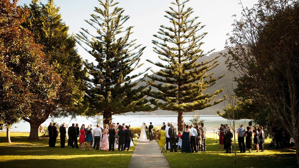 A bride and groom get married at Furneaux Lodge with Endeavour Inlet background in the Marlborough Sounds in New Zealand's top of the South Island