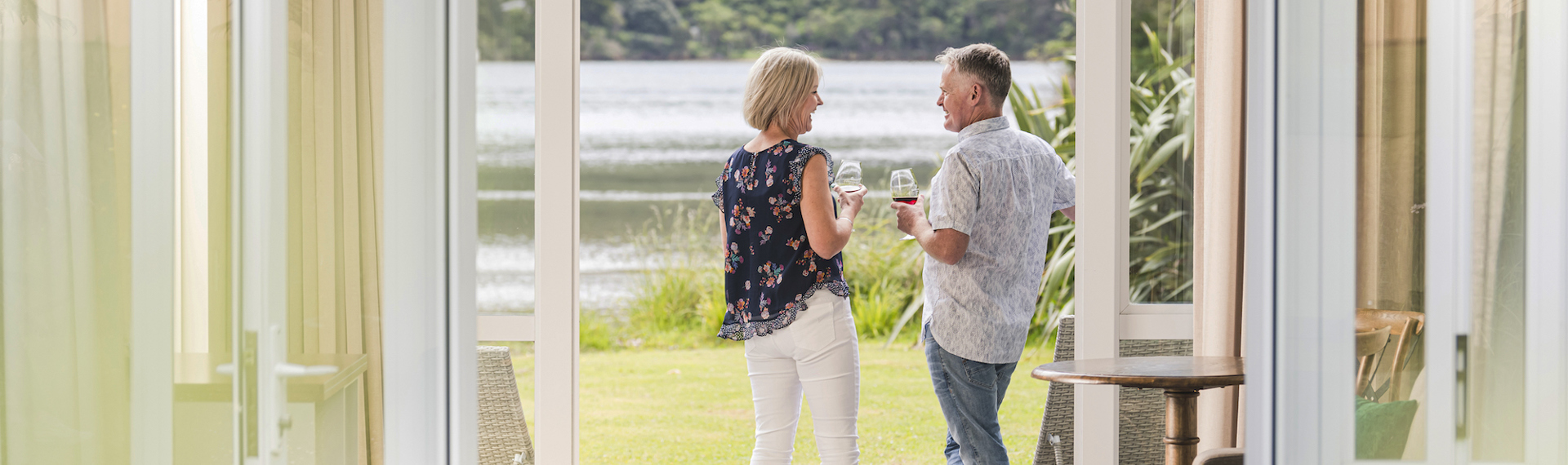 A couple enjoying glasses of Pinot Noir outside on an Endeavour Suite Rows of wine glasses on a shelf at the Furneaux Lodge  in the Marlborough Sounds at the top of New Zealand's South Island.