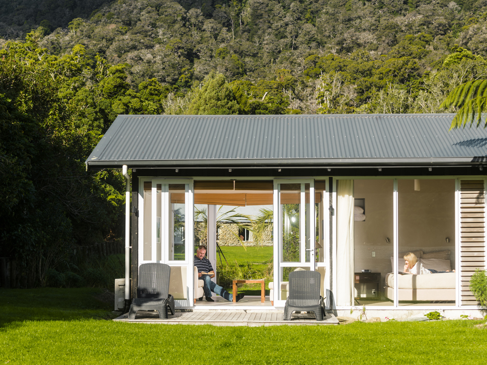 A women reads a book on the bed and a man reads in the living area of an Endeavour Suite at Furneaux Lodge in the Marlborough Sounds, New Zealand.